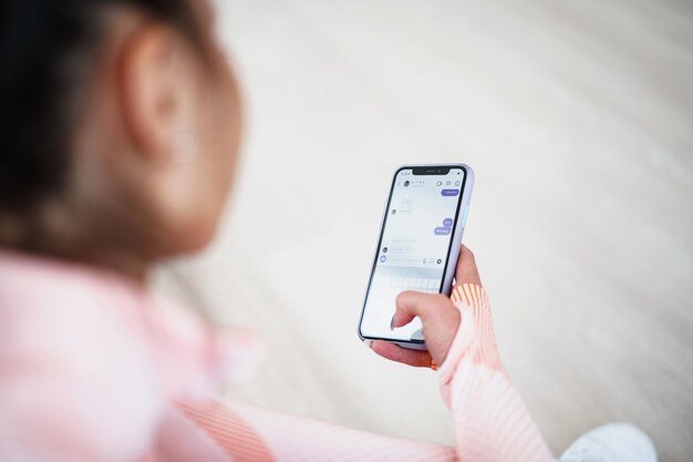 Schöne junge Frau in Sportkleidung, die drinnen sitzt und vor dem Training auf das Smartphone schaut