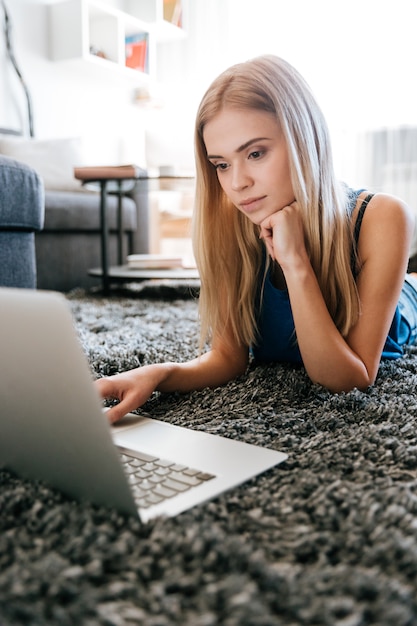 Kostenloses Foto schöne junge frau liegend und mit laptop auf teppich