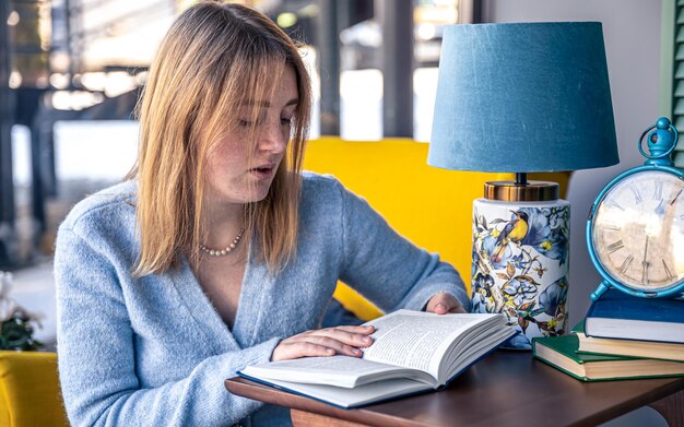 Schöne junge Frau liest ein Buch, während sie am Tisch sitzt