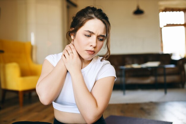 Schöne junge Frau mit besorgtem frustriertem Blick, der Hände um ihren Hals hält, der Schmerz fühlt