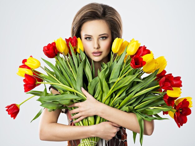 Schöne junge Frau mit Blumen in den Händen. Hübsches Mädchen hält die roten Tulpen