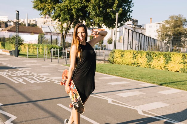 Schöne junge Frau mit dem Skateboard, das auf Straße steht