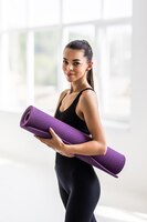 Schöne junge frau mit einer yogamatte im fitnessstudio