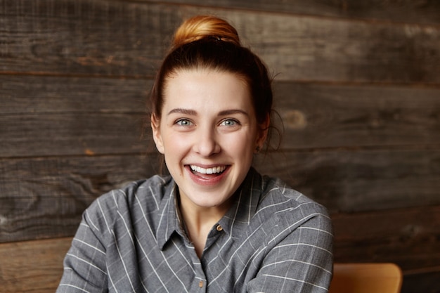 Kostenloses Foto schöne junge frau mit haarknoten mit freudigem blick, fröhlich lächelnd, glücklich mit einigen positiven nachrichten