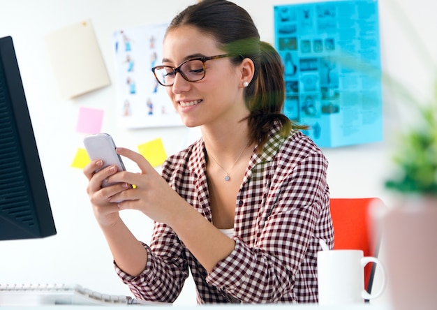 Schöne junge Frau mit ihrem Handy im Büro.