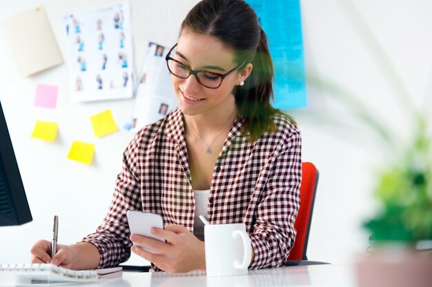 Schöne junge Frau mit ihrem Handy im Büro.