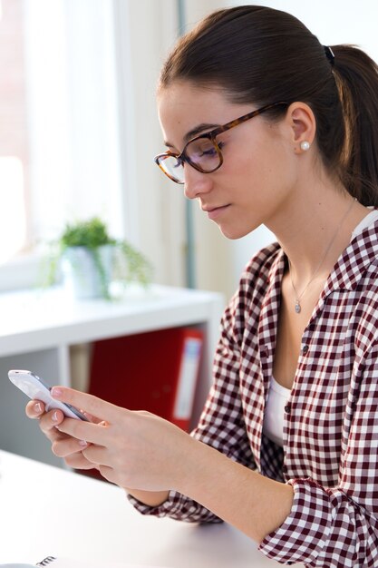 Schöne junge Frau mit ihrem Handy im Büro.