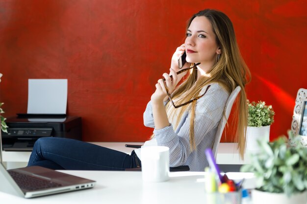 Schöne junge Frau mit ihrem Handy im Büro.