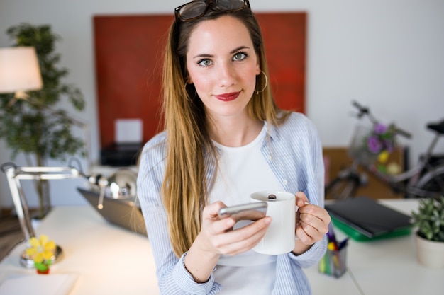 Schöne junge Frau mit ihrem Handy im Büro.