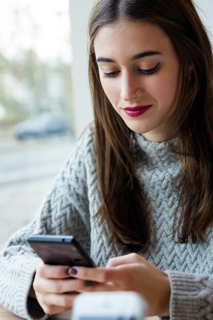 Schöne junge Frau mit ihrem Handy in Kaffee.