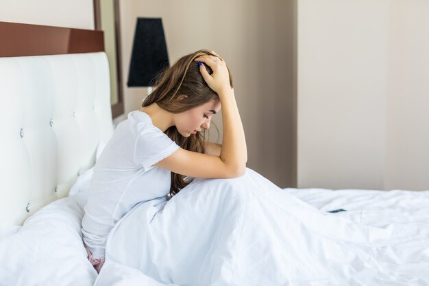 Schöne junge Frau mit Kopfschmerzen im Bett sitzend sitting