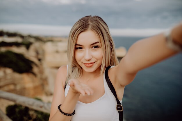 Schöne junge Frau nehmen Selfie vom Telefon senden Kissis an der Spitze der schönen Klippen und Felsen