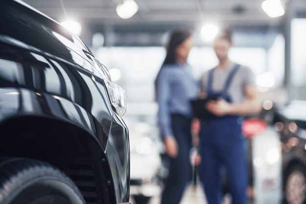 Schöne junge Frau spricht mit hübschem Automechaniker, während ein Auto im Autohaus repariert wird