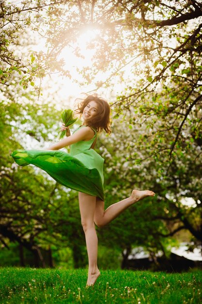 Schöne junge Frau springt in einen grünen Garten