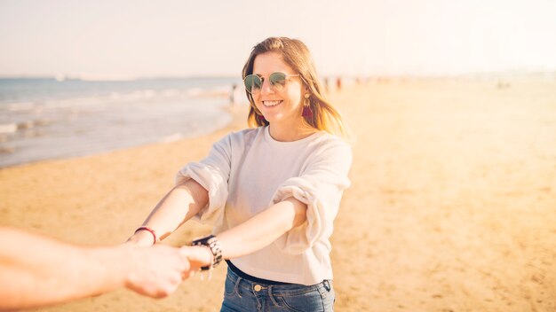 Schöne junge Frau, welche die Hand ihres Freundes am Strand hält