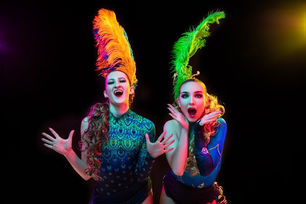 Schöne junge Frauen im Karnevals- und Maskeradenkostüm in den bunten Neonlichtern auf schwarzer Wand