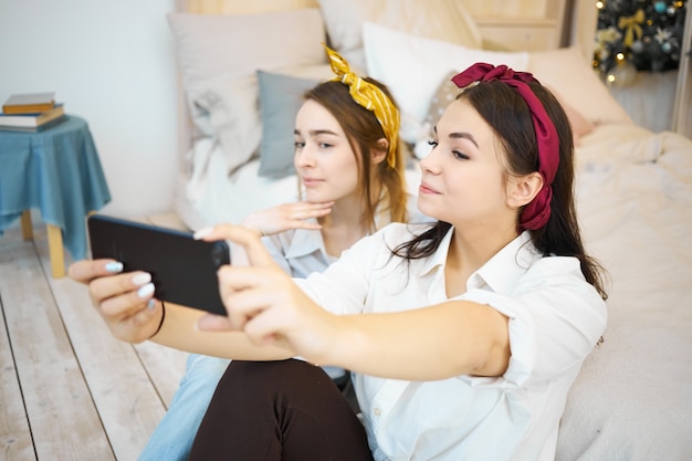 Schöne junge Freundinnen, die zu Hause zusammen entspannen und Selfie nehmen