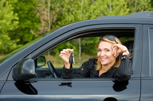 Schöne junge glückliche Frau im neuen Auto mit Schlüsseln - draußen