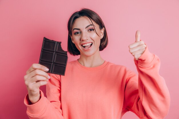 Schöne junge glückliche Frau mit Schokoriegel auf rosa Hintergrund und hellem Make-up