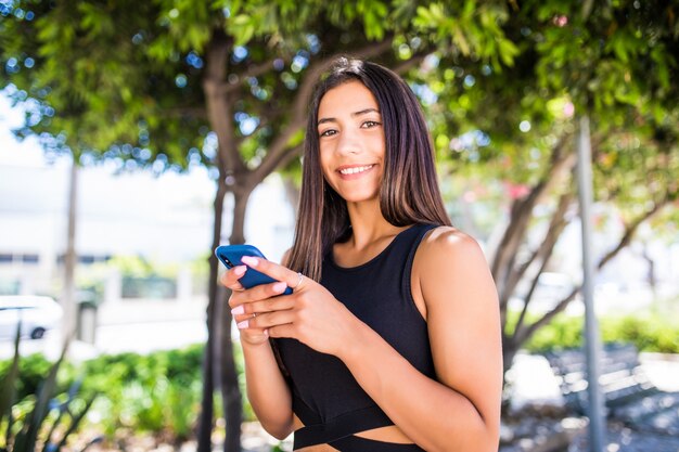 Schöne junge glückliche lateinische Frau, die auf Handy auf Stadtstraße SMS schreibt. Studentin, die im Winter auf der Stadtstraße im Freien auf dem Handy geht und eine SMS sendet.