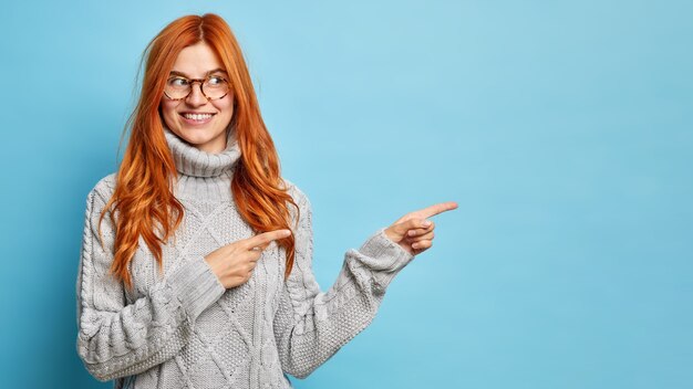 Schöne junge Ingwerfrau, die auf Kopienraum zeigt