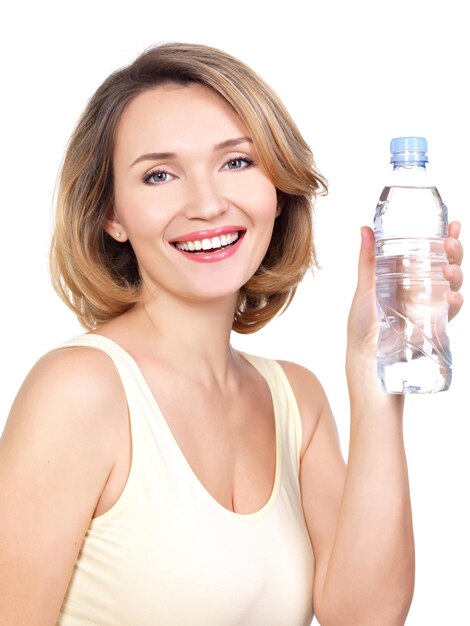 Schöne junge lächelnde Frau mit einer Flasche Wasser auf einer weißen Wand.