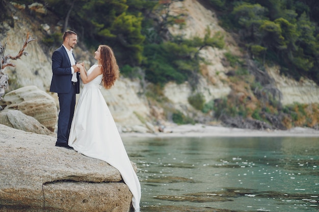 schöne junge langhaarige Braut im weißen Kleid mit ihrem jungen Ehemann nahe Fluss