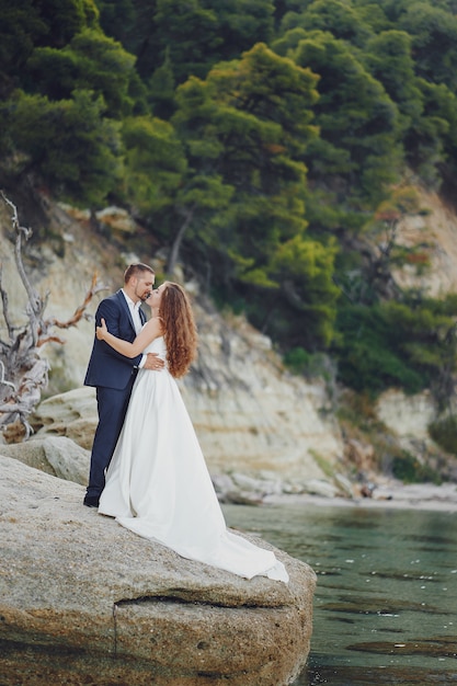 schöne junge langhaarige Braut im weißen Kleid mit ihrem jungen Ehemann nahe Fluss