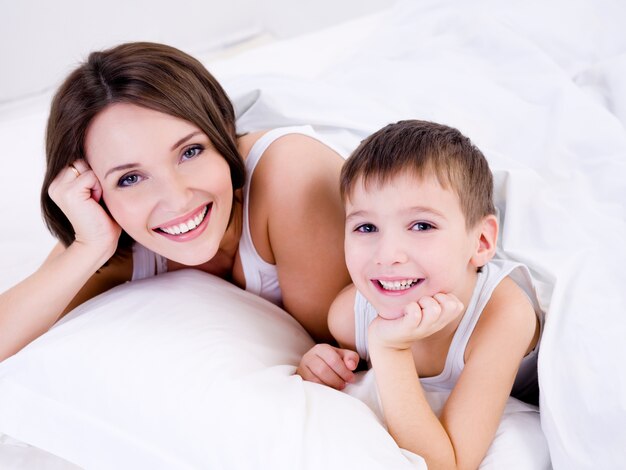 Schöne junge Mutter mit ihrem kleinen Jungen, der auf einem Bett liegt