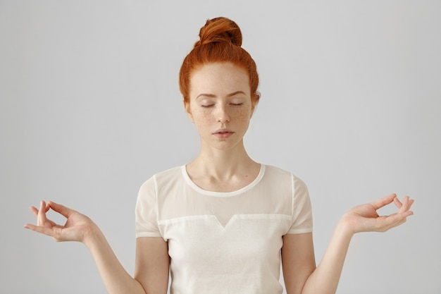 Kostenloses Foto schöne junge rothaarige frau, die yoga am morgen drinnen an der weißen wand tut