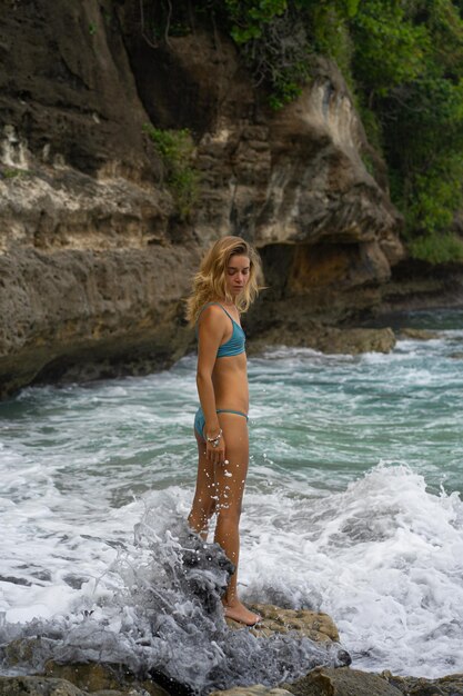 Schöne junge schlanke Frau mit langen blonden Haaren in einem Badeanzug am Strand in der Nähe des Ozeans. Am Strand entspannen. Tropischer Urlaub.