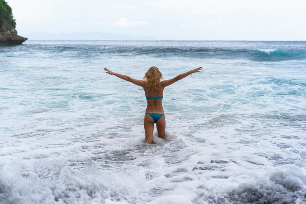 Schöne junge schlanke Frau mit langen blonden Haaren in einem Badeanzug am Strand in der Nähe des Ozeans. Am Strand entspannen. Tropischer Urlaub.