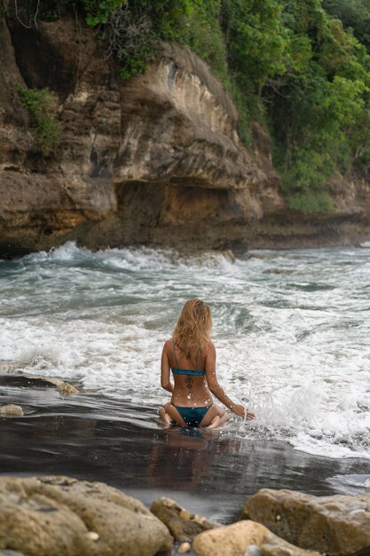 Schöne junge schlanke Frau mit langen blonden Haaren in einem Badeanzug am Strand in der Nähe des Ozeans. Am Strand entspannen. Tropischer Urlaub.