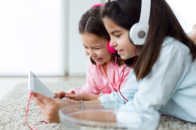 Schöne junge Schwestern hören Musik mit digitaler Tablette a