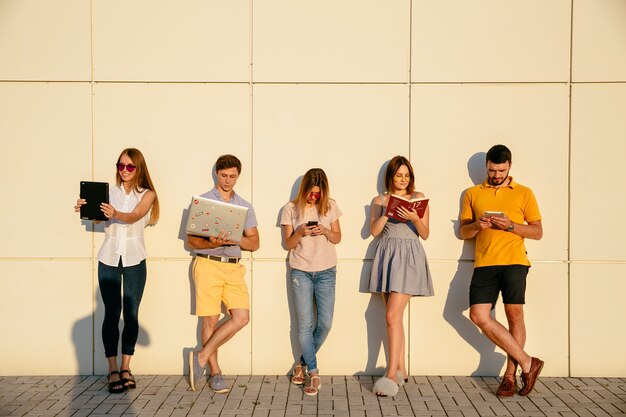 Schöne junge Studenten benutzen Geräte, Lesebuch und Lächeln