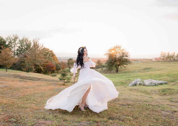 Schöne kaukasische brünette Braut tanzt auf der vergilbten Wiese im warmen Herbstabend
