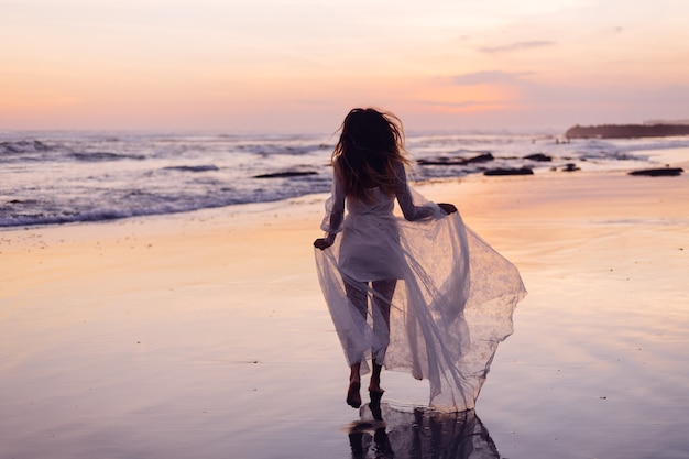 Schöne kaukasische Frau allein im weißen Kleid am lila Sonnenuntergang durch Ozean