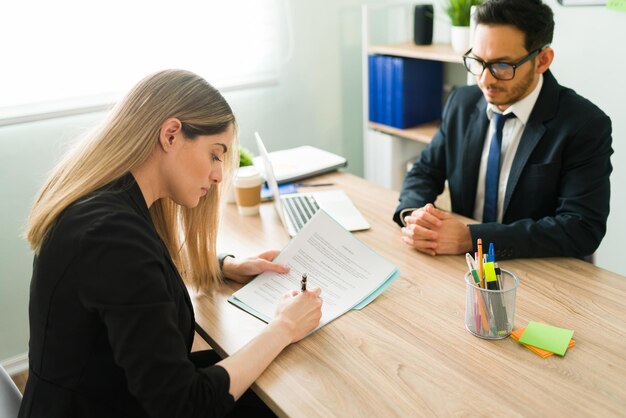 Schöne kaukasische Frau, die einen Arbeitsvertrag unterzeichnet, um einen neuen Job in einer Unternehmenszentrale zu beginnen. Professioneller männlicher Chef, der ein Geschäft mit einer Kundin abschließt