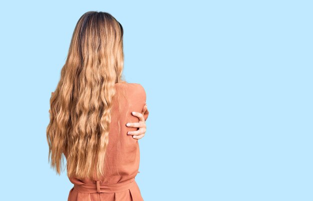 Schöne kaukasische Frau mit blonden Haaren im Sommeroverall, die sich glücklich und positiv von hinten umarmt. Selbstliebe und Selbstfürsorge