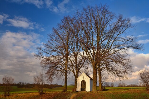 Schöne kleine Kapelle mit Landschaft und Bäumen bei Sonnenuntergang. Nebovidy - Tschechische Republik.