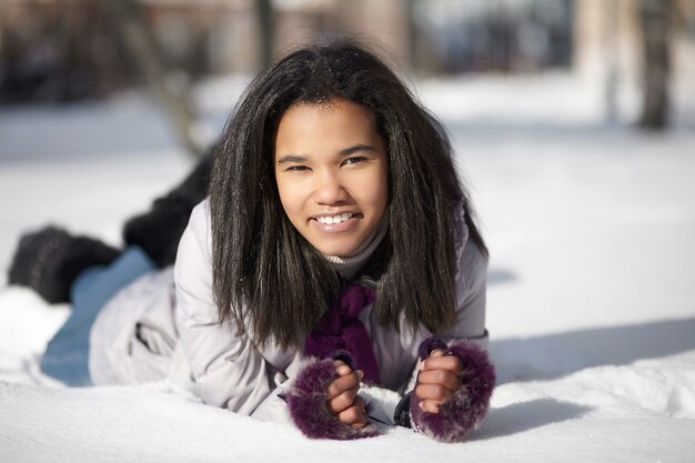 Schöne lächelnde amerikanische schwarze Frau, die draußen im Schnee liegt