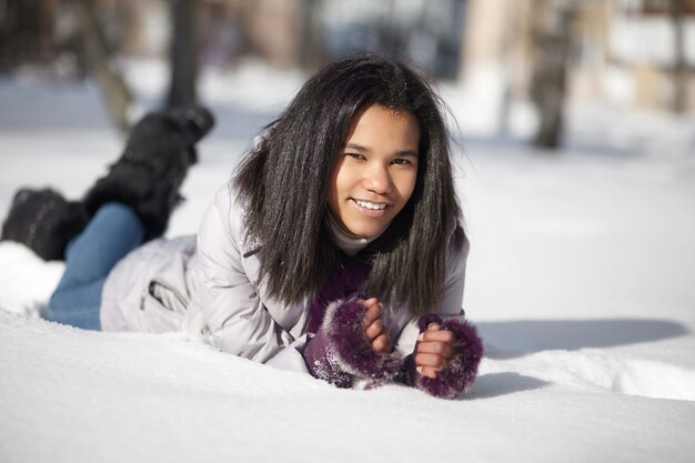 Schöne lächelnde amerikanische schwarze Frau, die draußen im Schnee liegt