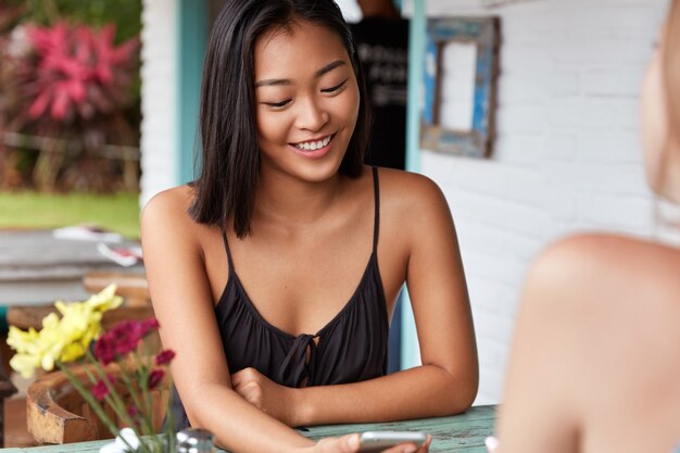 Schöne lächelnde asiatische Frau, die beiläufig auf einem Kaffeehaus gekleidet ist