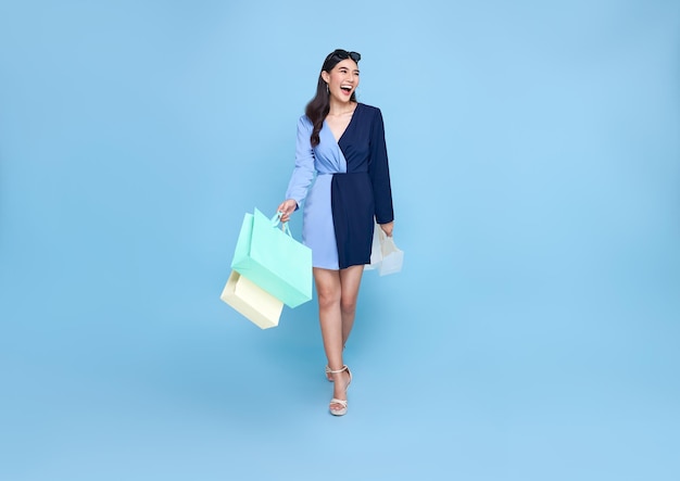 Schöne lächelnde asiatische Shopaholic-Frau mit Einkaufstüten, die zum Sommerschlussverkauf geht