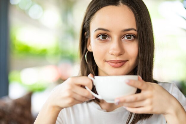 Schöne lächelnde Frau, die Kaffee im Café trinkt. Porträt einer reifen Frau in einer Cafeteria, die heißen Cappuccino trinkt und die Kamera betrachtet. Hübsche Frau mit Tasse Kaffee.