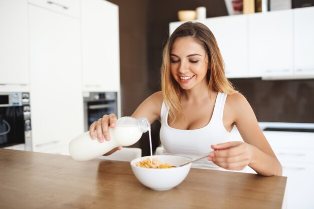 Schöne lächelnde junge Frau, die am Esstisch sitzt, der Frühstück hat