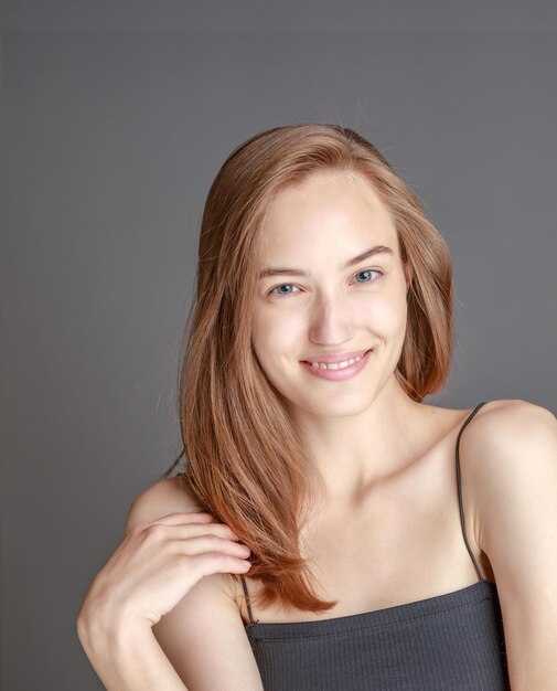 Schöne lächelnde junge Frau mit perfektem Hautgesicht natürliches Schönheitskonzept isoliert auf grauem Studiohintergrund