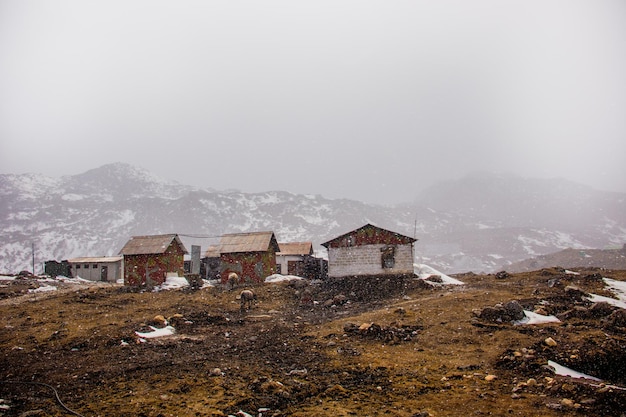 Kostenloses Foto schöne ländliche landschaft mit hütten gegen neblige berge unter dem schneefall