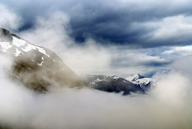 Schöne Landschaft einer Bergkette bedeckt mit Schnee unter weißen Wolken in Norwegen