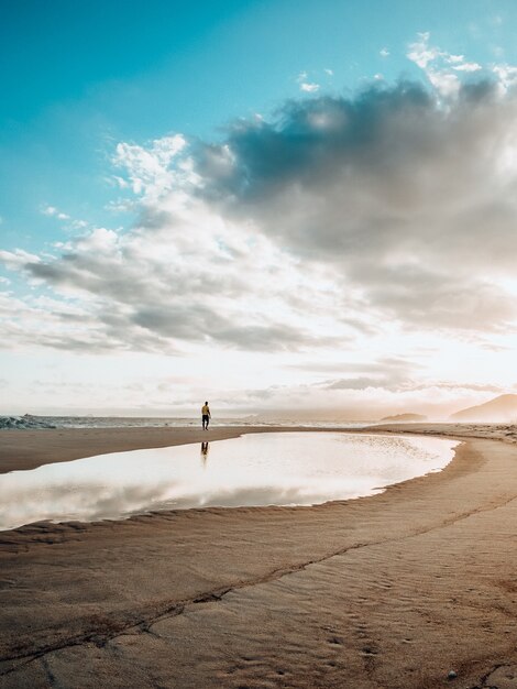 Schöne Landschaft einer Solo-Person, die während des Sonnenuntergangs am Strand mit einem bewölkten Himmel ausübt